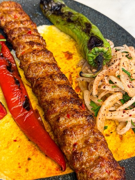 Kömür ateşinde pişmiş kebap, közlenmiş biber ve soğan piyazı